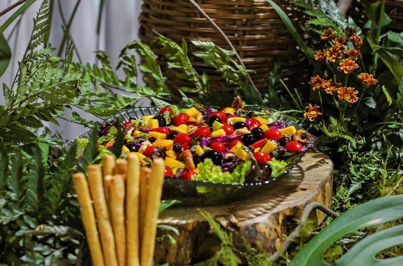 Salada colorida com folhas, manga e tomate servida em aparador decorado com folhagens