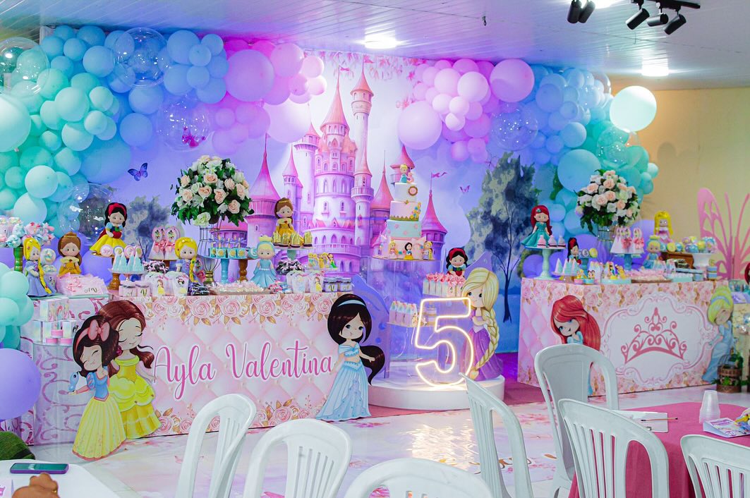 Salão montado para festa infantil de princesas, com painel de castelo, balões pastel e mesa do bolo