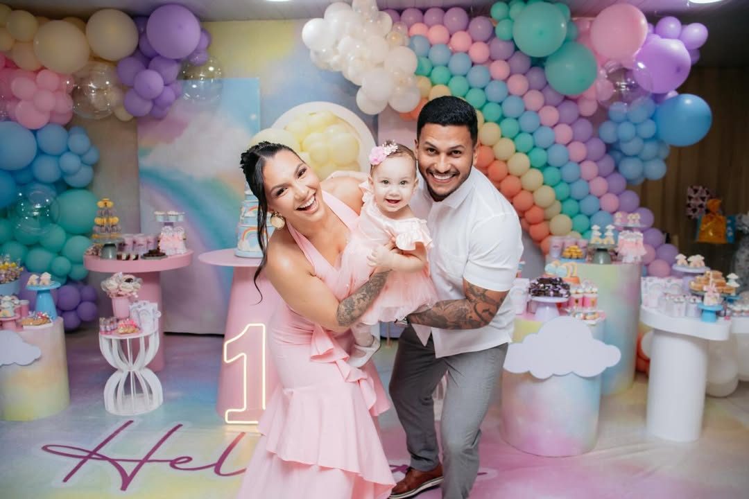 Família sorrindo em festa de 1 ano com arco-íris de balões pastel