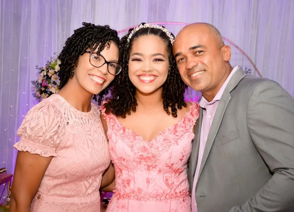 Debutante de vestido rosa sorrindo entre o pai e a mãe na festa de 15 anos