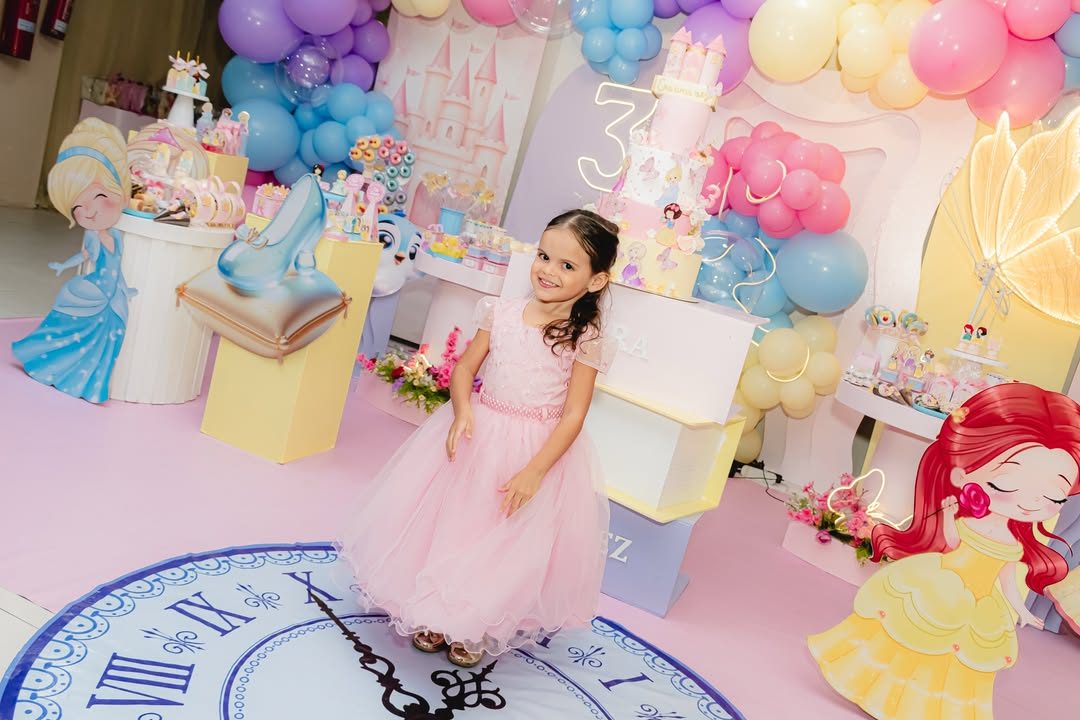 Menina de vestido rosa em festa de princesas, com castelo e balões ao fundo
