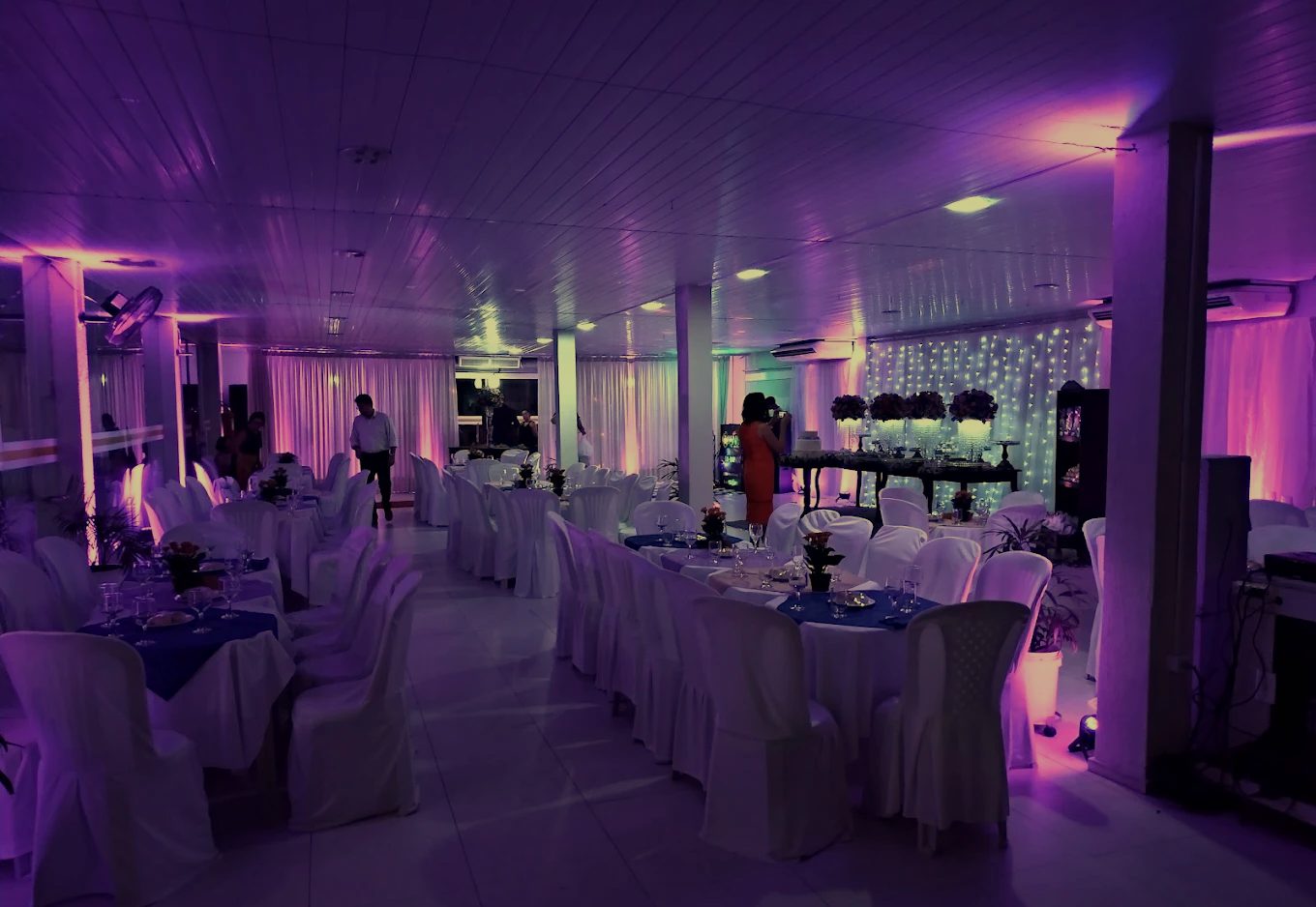 Salão de festas do Mona's Recepções à noite, com mesas vestidas e iluminação quente
