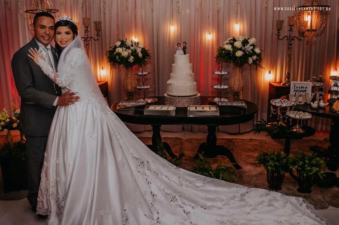 Noiva de véu longo ao lado da mesa do bolo, com luz quente